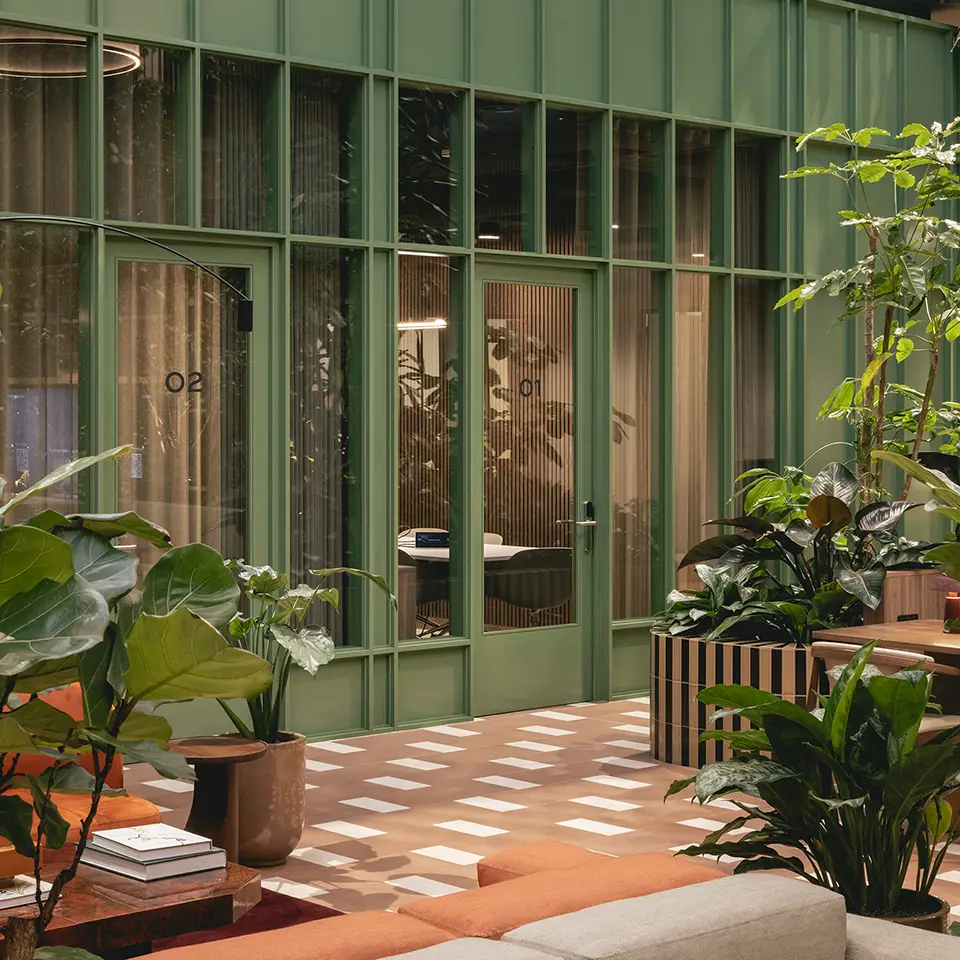 Green-framed meeting rooms seen from the atrium with sofa seating and plants in the foreground